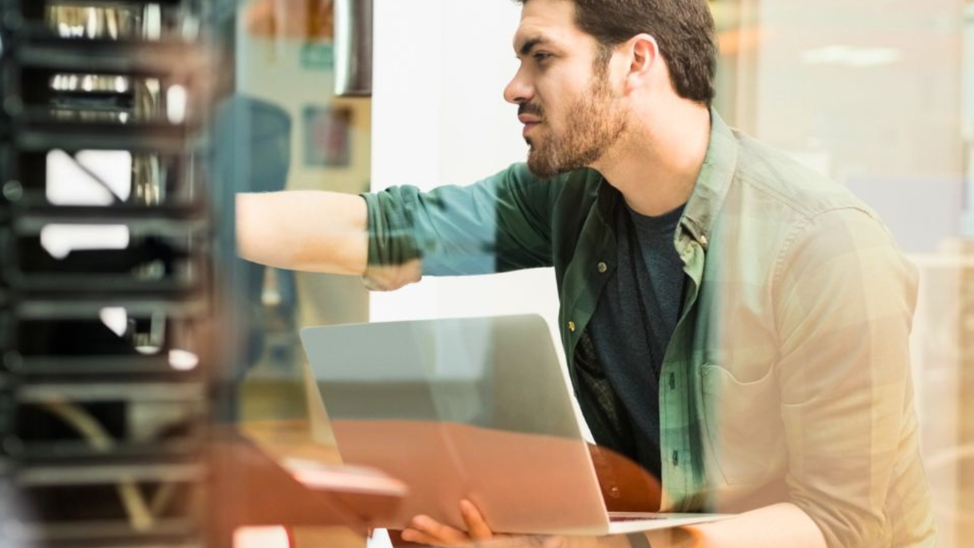 Person mit grünem Hemd arbeitet an Laptop vor einem Serverrack in einem modernen Büro
